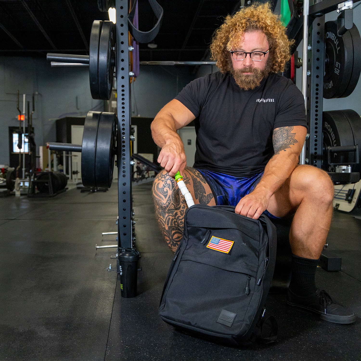 Man sitting on a bench in a squat rack pulling out a Little Stick from his backpack.