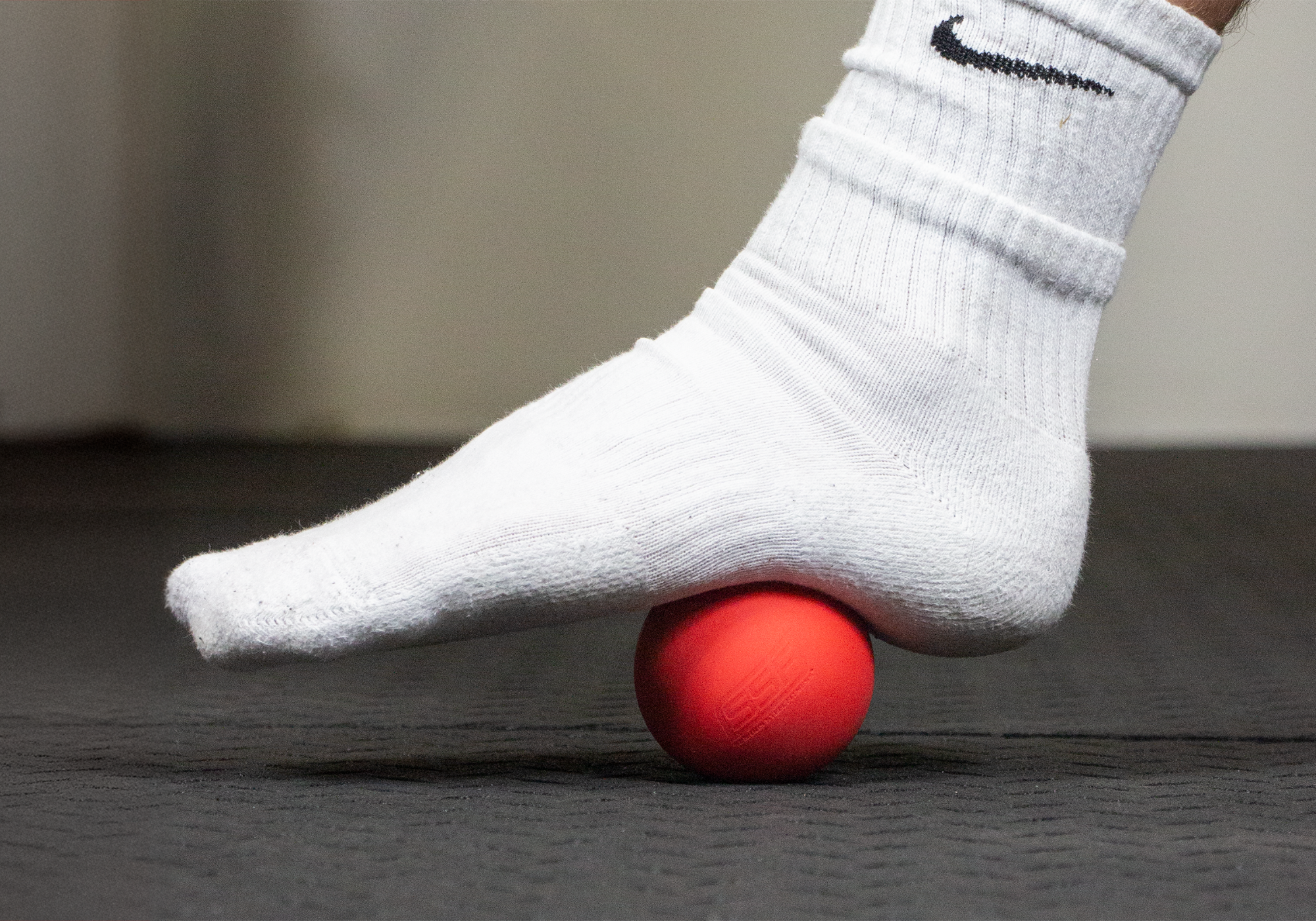 Foot wearing a sock while standing on the Lacrosse Ball to massage the sole of their feet on the ground.