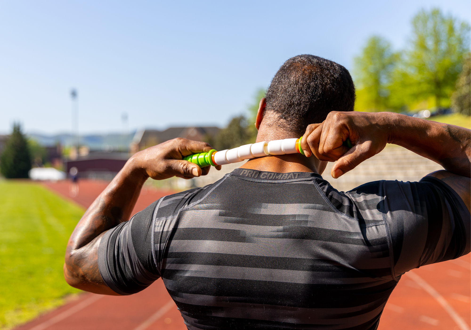 Athletic build male outside on a track using the Little Stick to massage their neck
