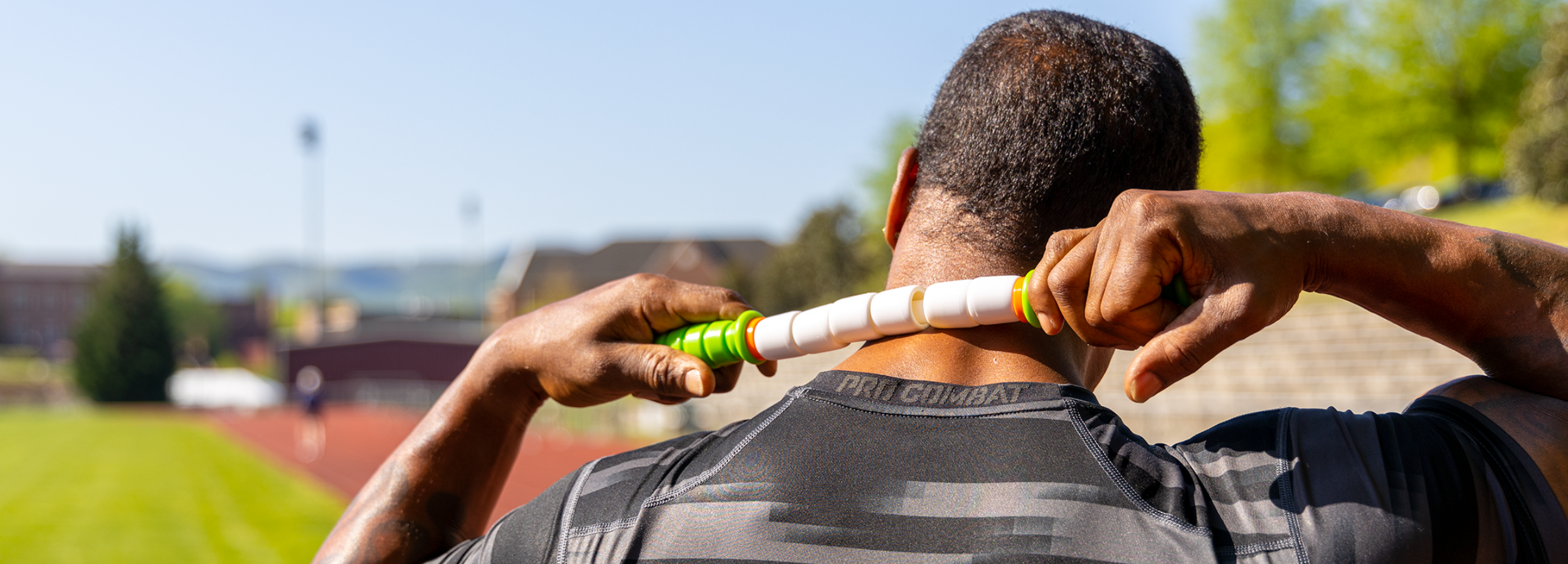 Athletic build male outside on a track using the Little Stick to massage their neck