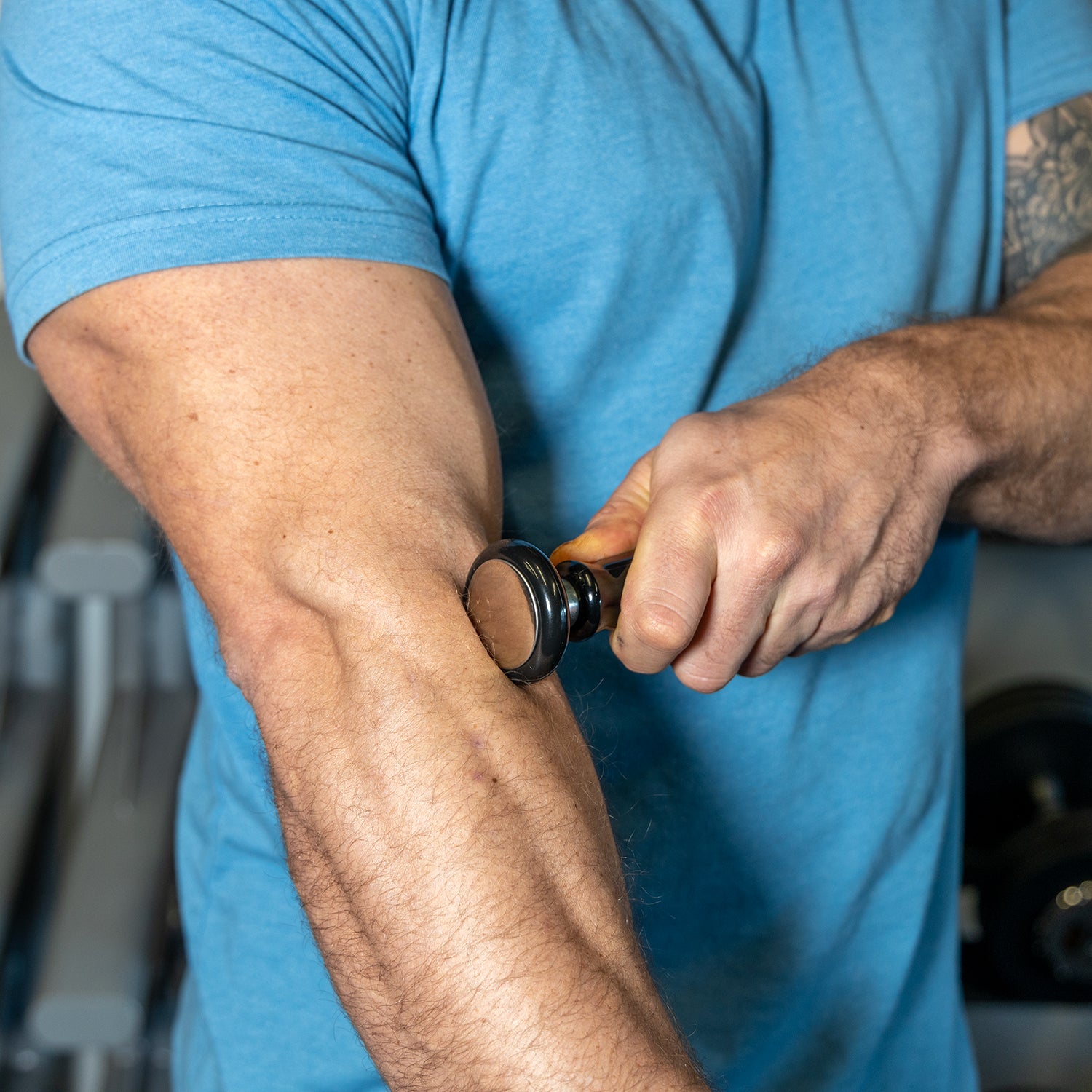 Man wearing a light blue shirt using the The Intruder to massage his right forearm extensor.