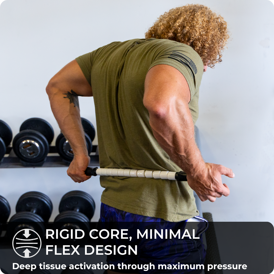 A muscular person with curly hair uses the Stiff Stick - 24 muscle roller on their lower back in a gym, dumbbells behind them. Text overlay: “Rigid core, minimal flex design. Deep tissue activation with maximum pressure.”.